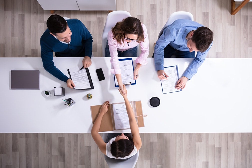 Overhead view of Businesswoman Shaking Hands with man across long table with group of employers Standing Out as a Job Candidate